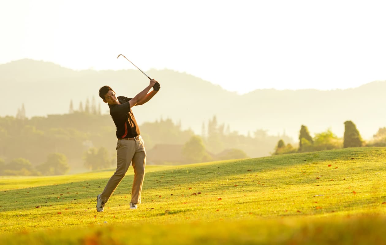 A golfer swinging in the afternoon sunlight